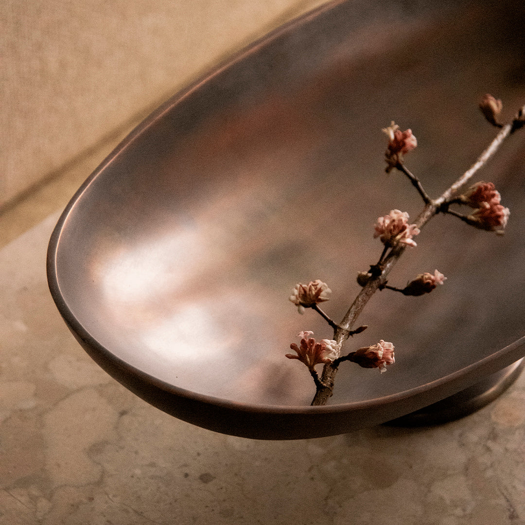 Elegant bronze bowl with a smooth finish, adorned with delicate pink cherry blossom branch accents.