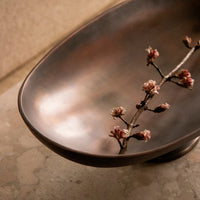 Elegant bronze bowl with a smooth finish, adorned with delicate pink cherry blossom branch accents.