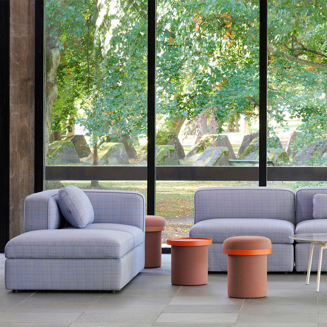 Blue plaid couches with round orange and pink accent tables against a green outdoor backdrop. Modern, vibrant design.