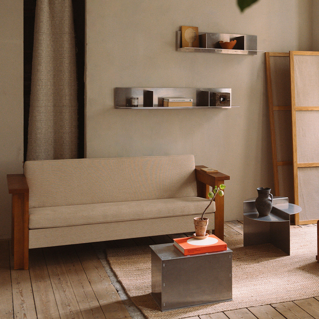Beige sofa with wooden arms, silver accent tables, and warm, neutral decor in a cozy, modern living space.
