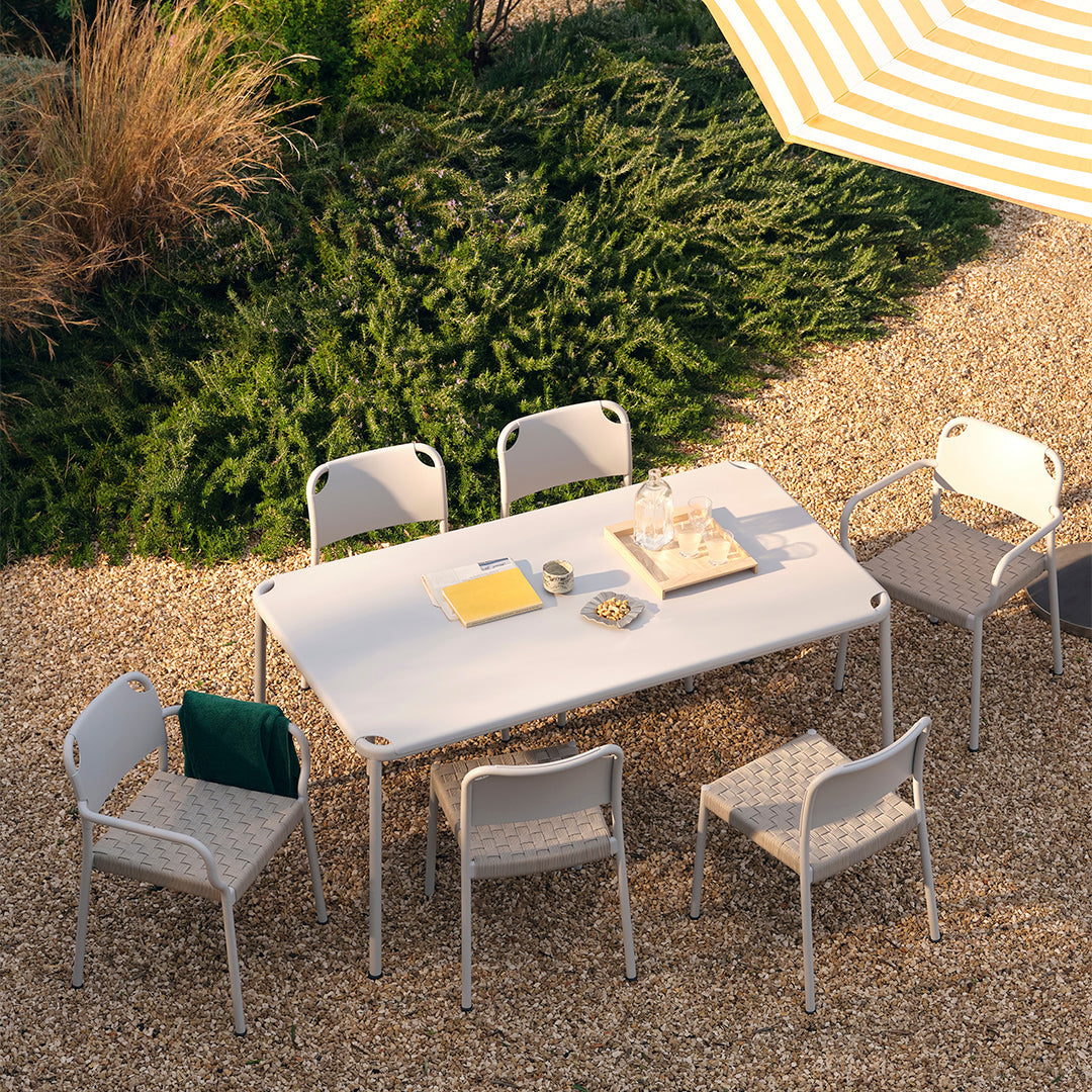 White outdoor table with gray patterned chairs, set in a natural landscape with green foliage and a yellow striped umbrella.