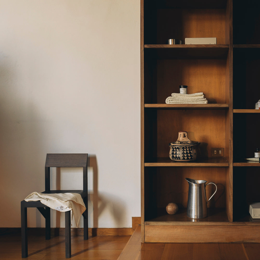 Minimalist black chair and wooden shelving unit with natural tones, showcasing neutral textiles and sleek metallic accents.