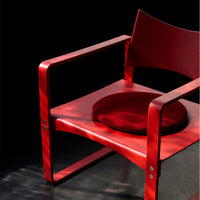Red wooden chair with a round red cushion, featuring sleek lines and a minimalist design against a dark background.