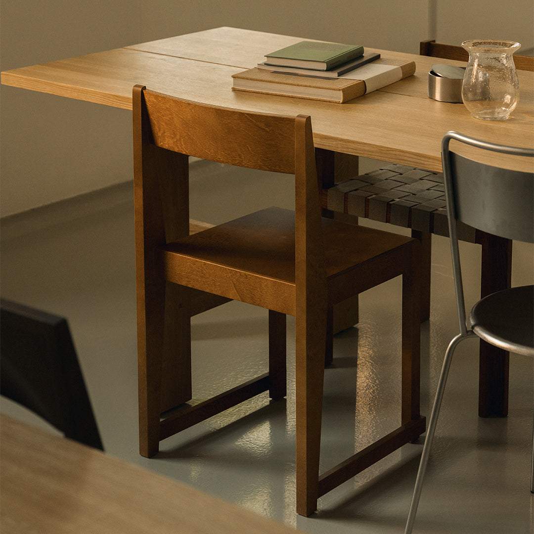 Natural wood dining chair with a sleek, minimalist design, paired with a warm-toned wooden table and neutral gray flooring.