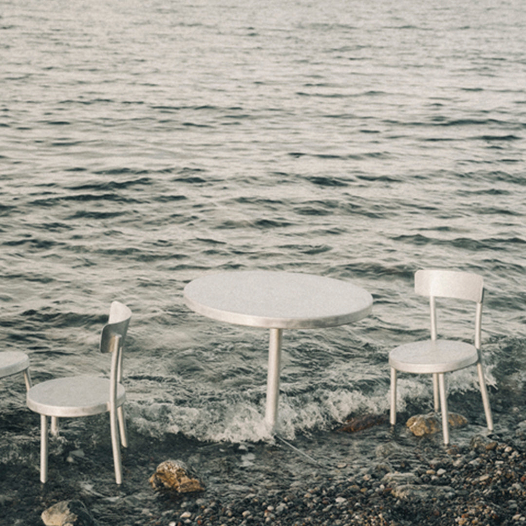 Silver metallic table and chairs set against a serene water backdrop, showcasing sleek, modern design and reflective surfaces.