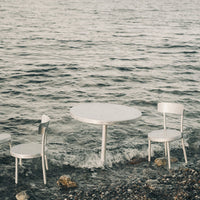 Silver metallic table and chairs set against a serene water backdrop, showcasing sleek, modern design and reflective surfaces.