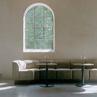 Elegant beige curved sofa with black accent tables, complemented by soft natural light through an arched window.