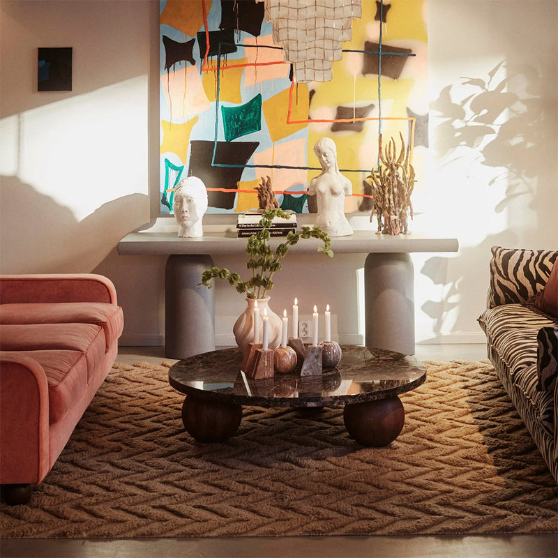 "Soft pink velvet sofa, zebra print cushions, earthy beige rug, and colorful abstract wall art with yellow, green, and black accents."