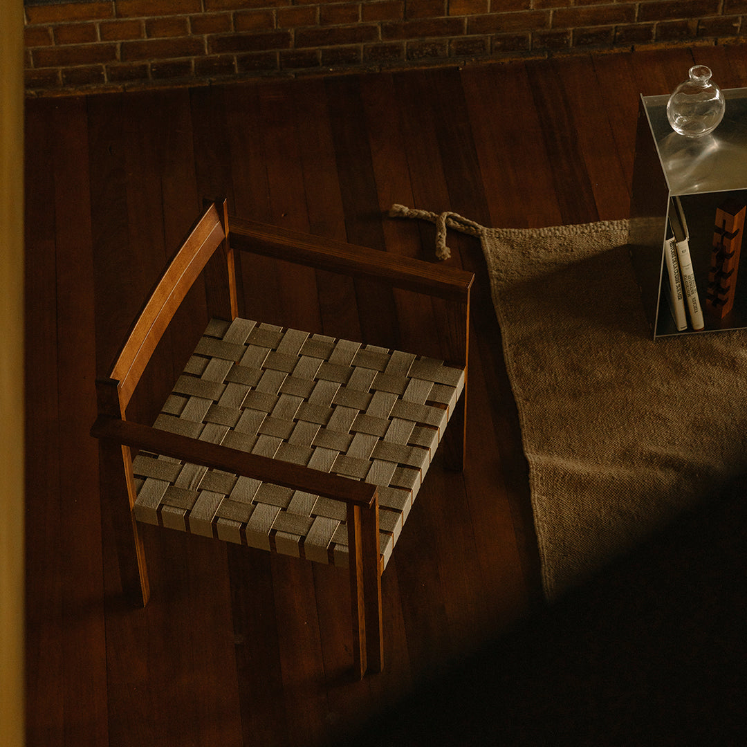 Wooden chair with a woven beige seat against a warm wooden floor, complemented by a textured rug.