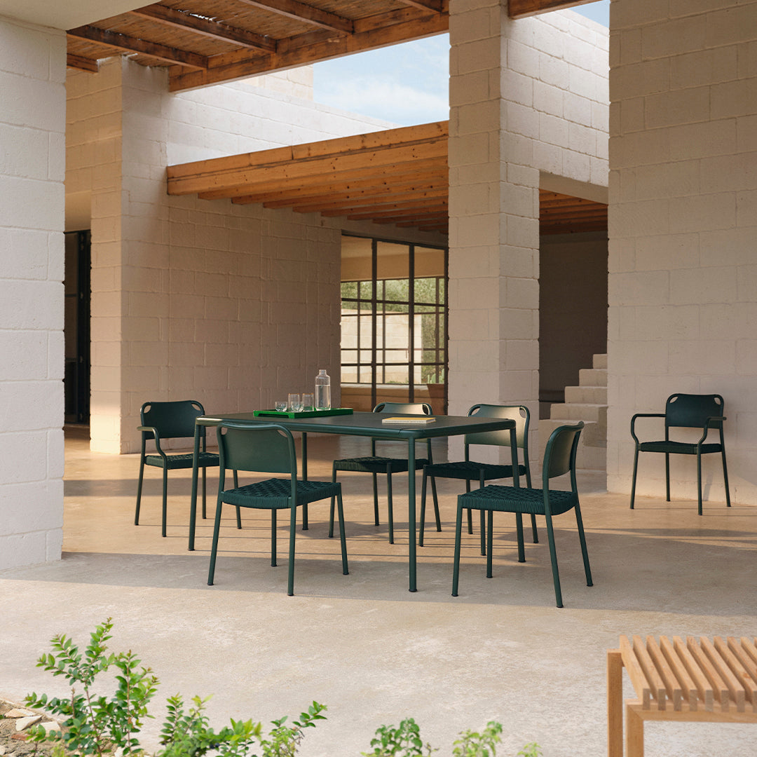 "Modern outdoor dining set in deep green with sleek lines, complemented by a natural stone floor and wooden accents."