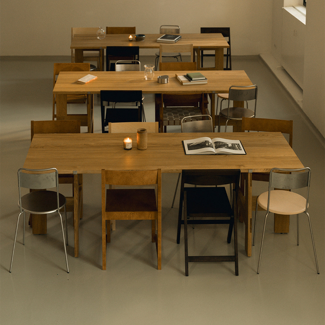 "Wooden tables with a natural finish, surrounded by various colorful chairs in black, silver, and muted tones."