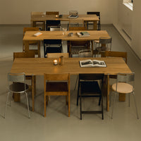 "Wooden tables with a natural finish, surrounded by various colorful chairs in black, silver, and muted tones."