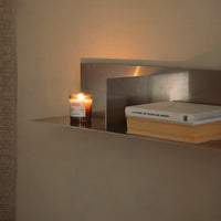 Metallic silver shelf with warm candlelight, complemented by soft beige wall and stacked neutral-colored books.