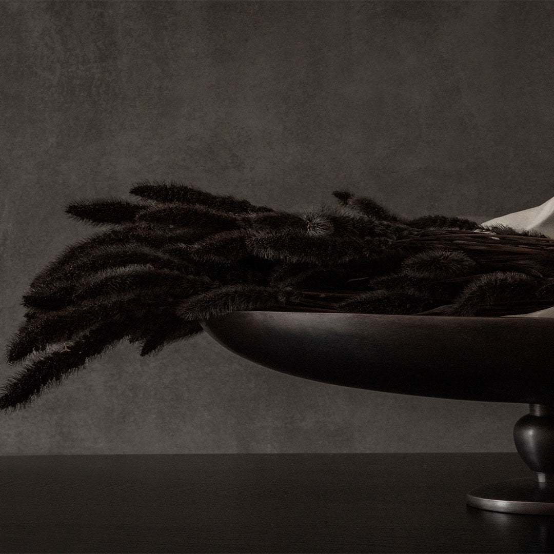 Dark textured stems in a sleek black bowl against a moody gray background, showcasing earthy elegance.