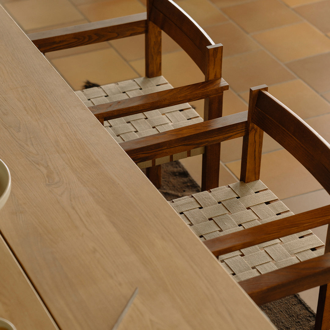"Natural wood chairs with woven beige seats, set on a warm, earthy-toned tiled floor."