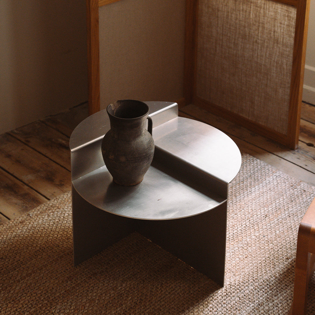 Round metal side table with a matte gray finish, featuring a sleek, modern design and soft, curved edges.