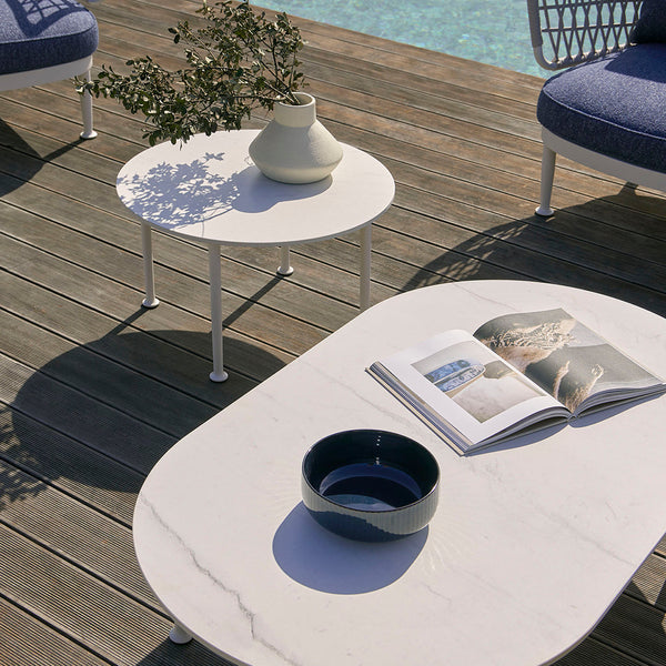 White marble coffee table with round edges, set against a wooden deck; features a blue bowl and magazine.