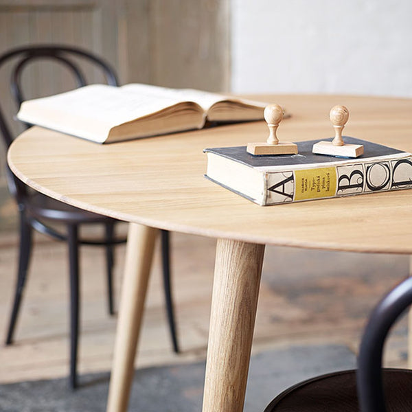 Natural wood round table with light oak finish, paired with sleek black chairs and neutral book covers.