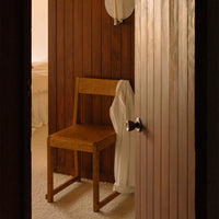 Wooden chair against warm wooden walls, with a cream-colored robe draped on it, creating a cozy, inviting atmosphere.