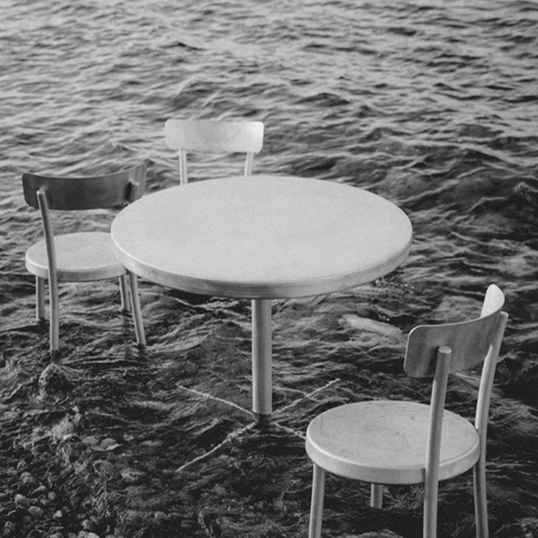 Minimalist black and white table and chairs partially submerged in water, showcasing smooth surfaces and simple design.