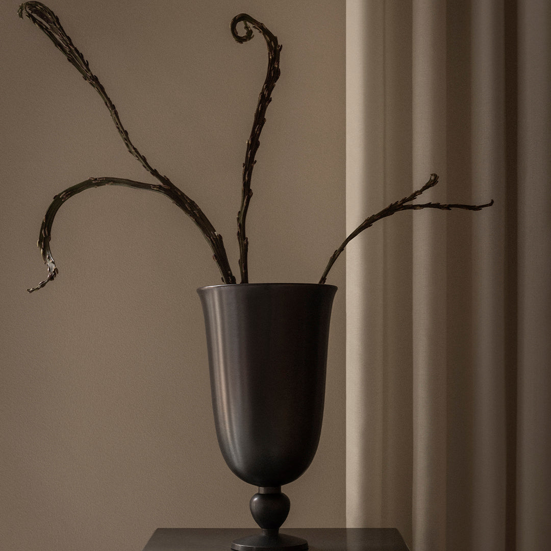 Elegant dark vase with textured surface, featuring slender, twisted branches against a neutral backdrop.