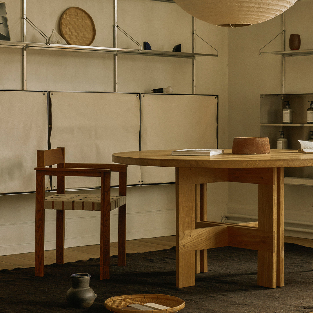 Wooden dining table with a natural finish, paired with a rustic brown chair, set against a neutral-toned backdrop.