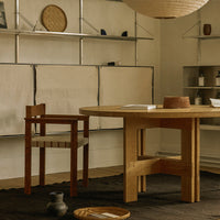 Wooden dining table with a natural finish, paired with a rustic brown chair, set against a neutral-toned backdrop.