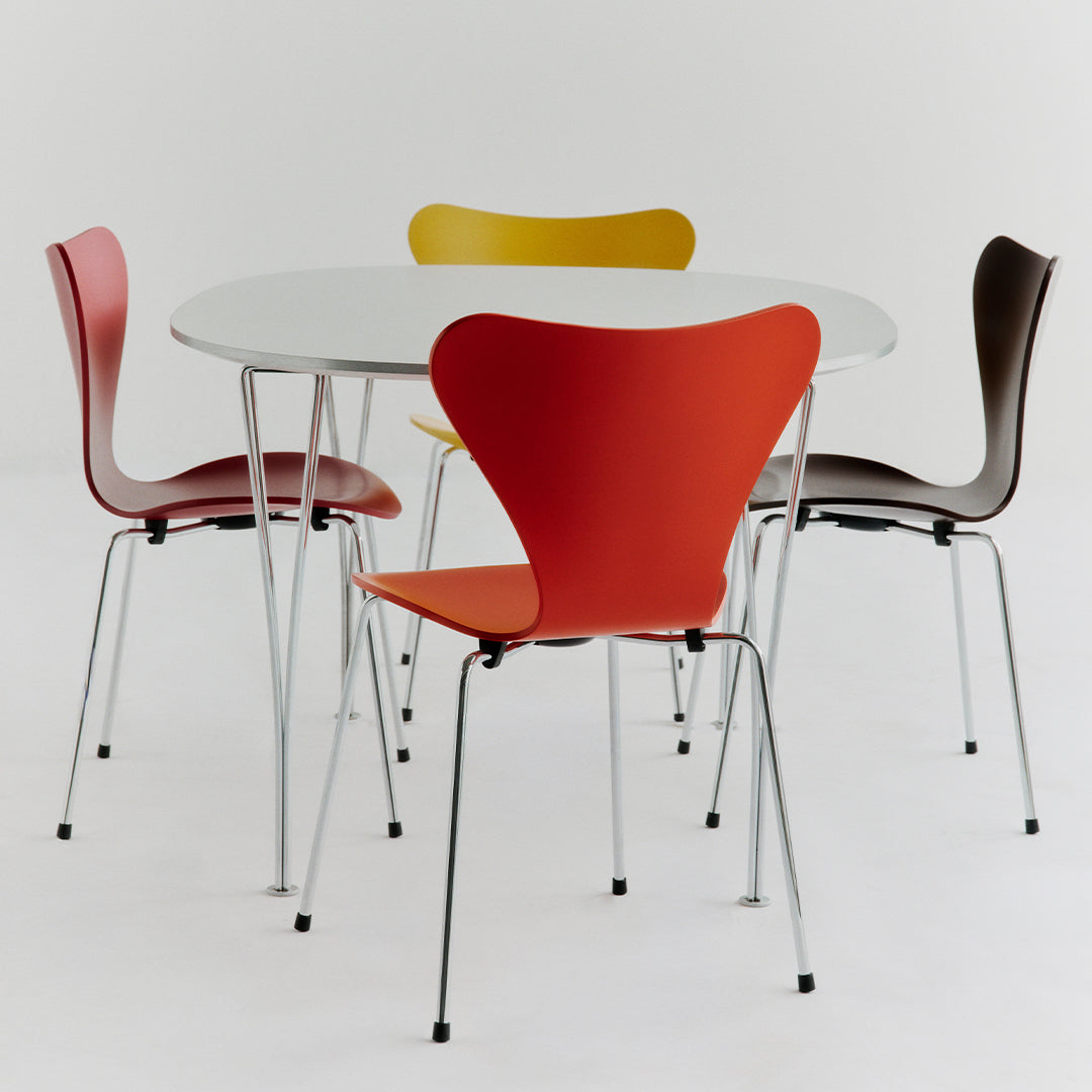 Colorful dining chairs in red, yellow, brown, and pink around a sleek white circular table. Modern design, vibrant hues.
