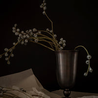 Dark metal vase with delicate gray floral stems against a black background, featuring subtle textures and elegant shapes.