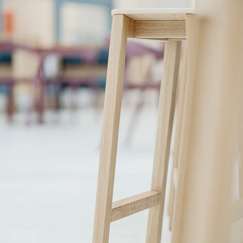 Light wood bar stool with smooth, natural grain pattern and soft, neutral background colors.