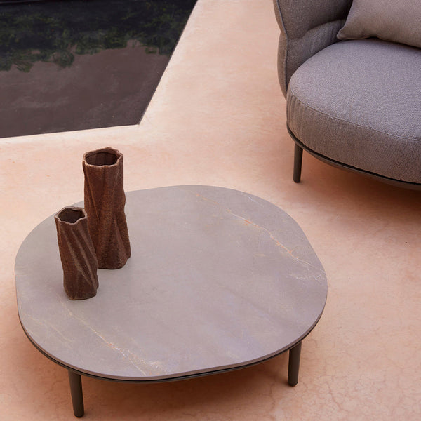 Gray organic-shaped coffee table with earthy brown vases on a soft peach background. Modern and minimalistic design.
