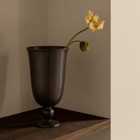 Black decorative vase with a smooth finish, featuring a single yellow flower and green bud on a subtle wooden shelf.