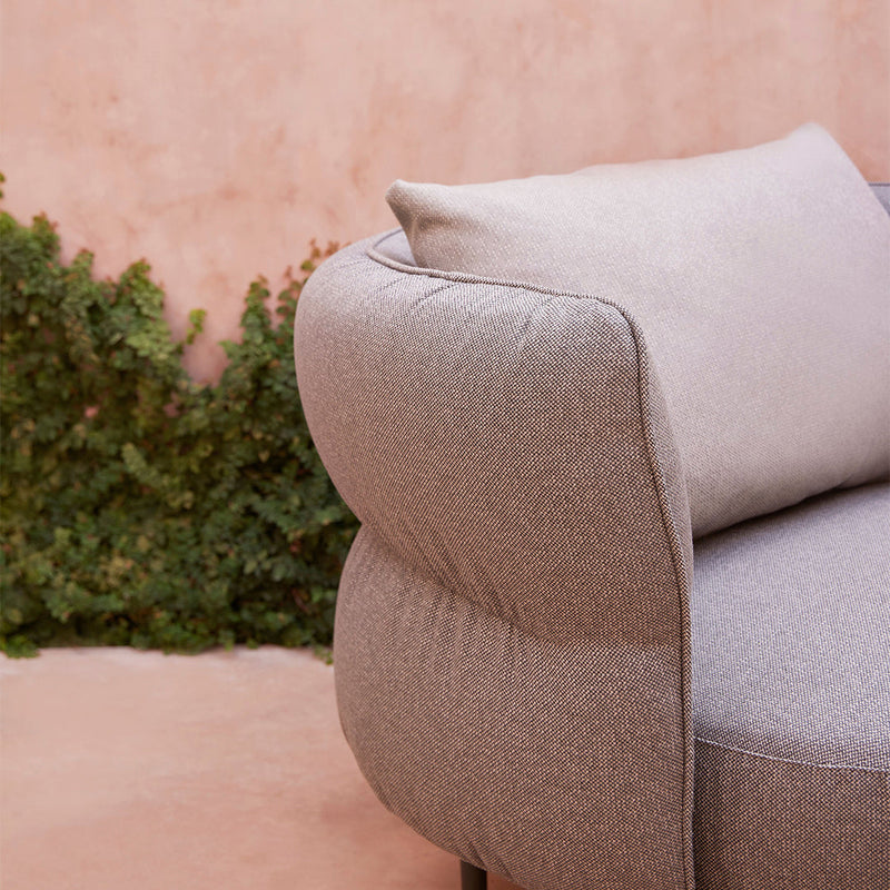 Light gray upholstered sofa with a smooth, textured pattern and a contrasting pale pink backdrop.