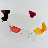 Modern oval dining table with a sleek white surface, surrounded by chairs in brown, red, and vibrant yellow.