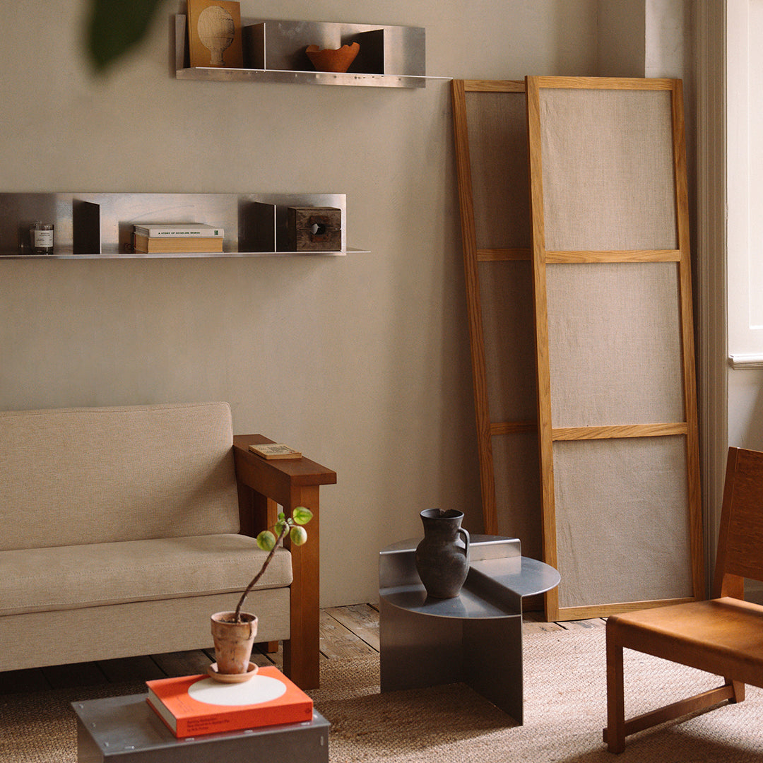 Neutral-toned living room with a beige sofa, wooden accents, and gray shelving; minimalistic design with soft patterns.