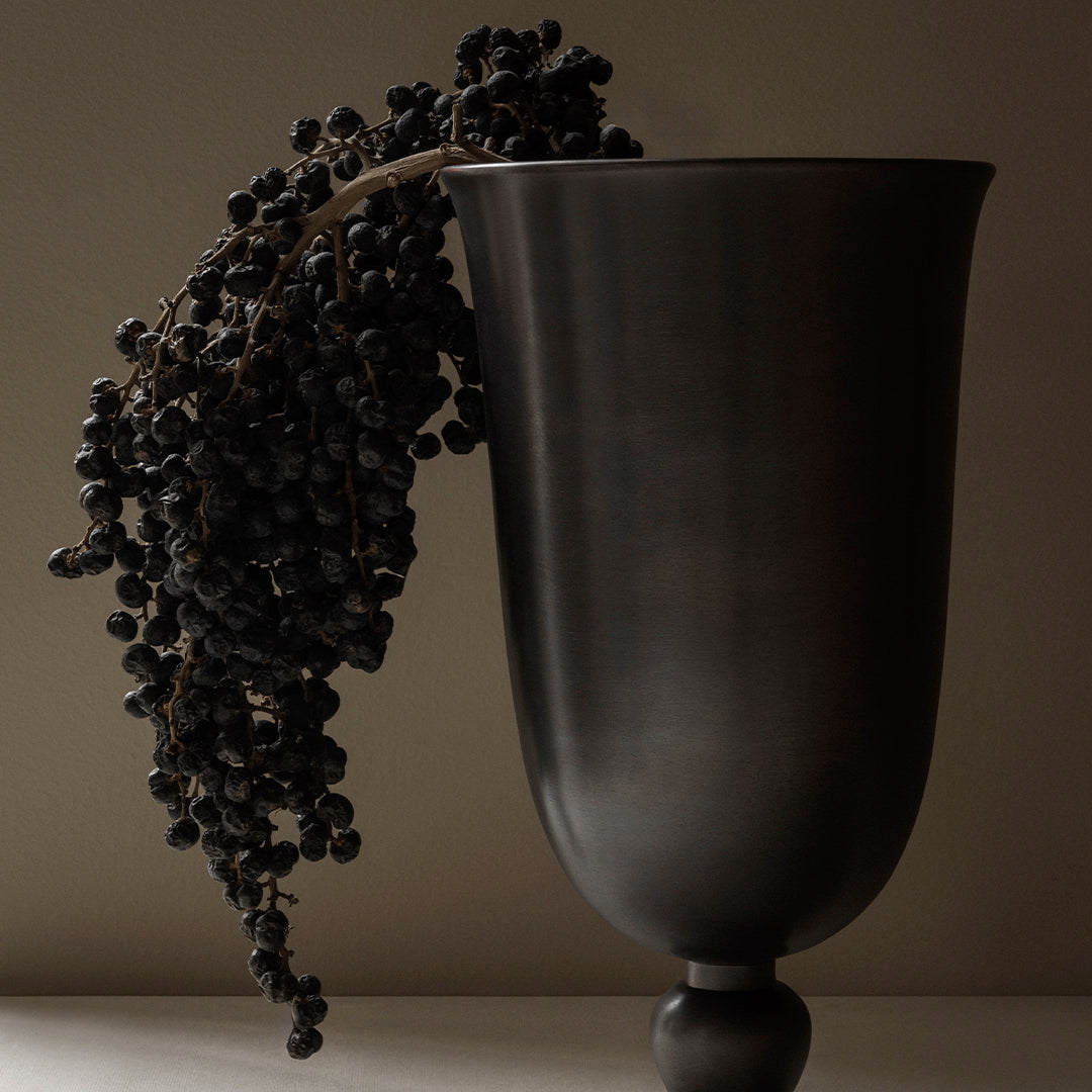 Black ceramic vase with a smooth finish, adorned with dark berries for a striking contrast against neutral backdrop.