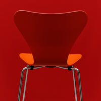 Red chair with an orange seat and sleek chrome legs, featuring a minimalist design. Perfect for modern decor.