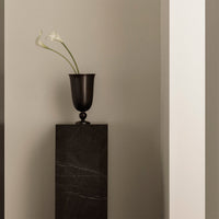 Black vase with white flowers on a dark stone pedestal against a neutral gray wall, showcasing elegant minimalism.