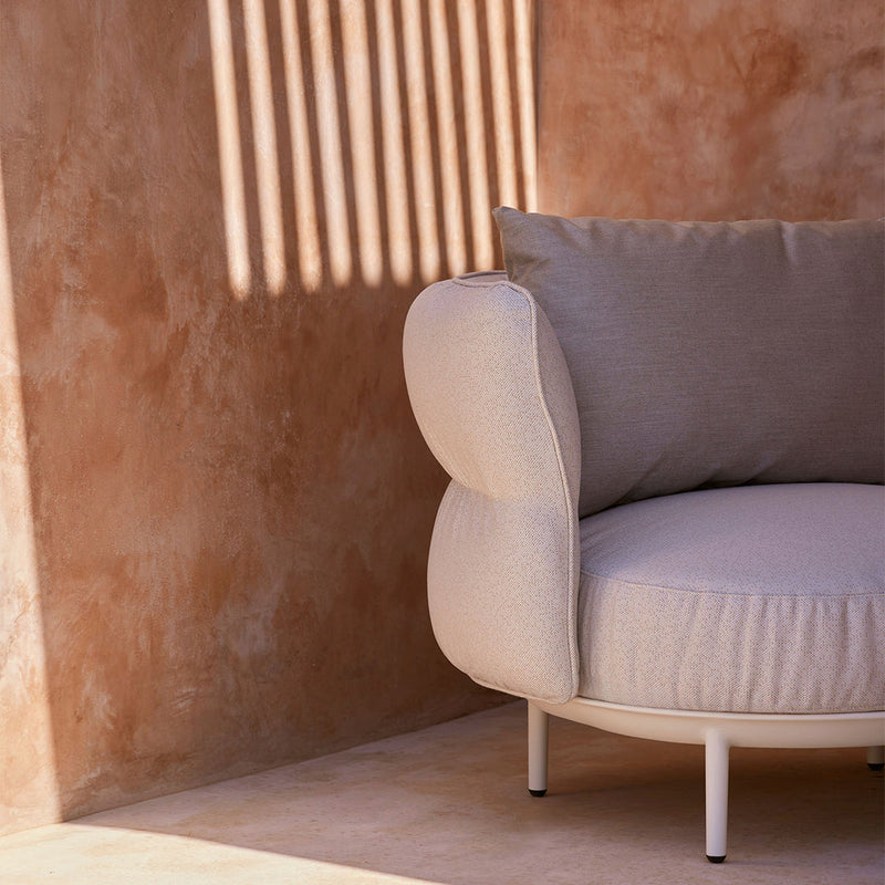 Light beige round sofa with a soft texture and a complementary gray cushion against a warm, earthy background.