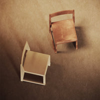 Two minimalistic chairs: one in creamy white, the other in warm brown, showcasing smooth finishes and clean lines.