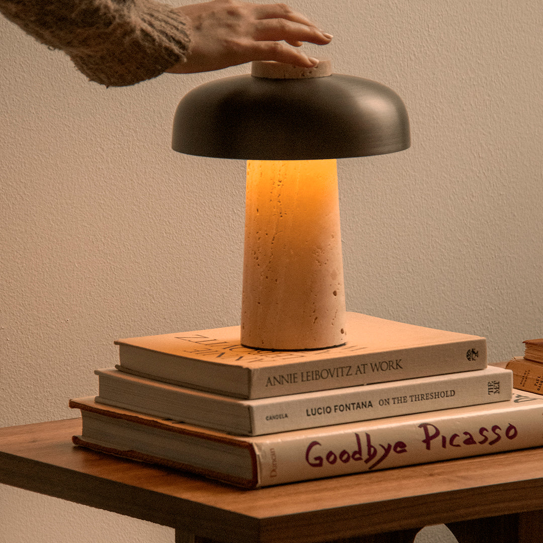 Modern lamp with a black metal shade, warm yellow glow, and a light wood base, topped with stacked neutral-colored books.