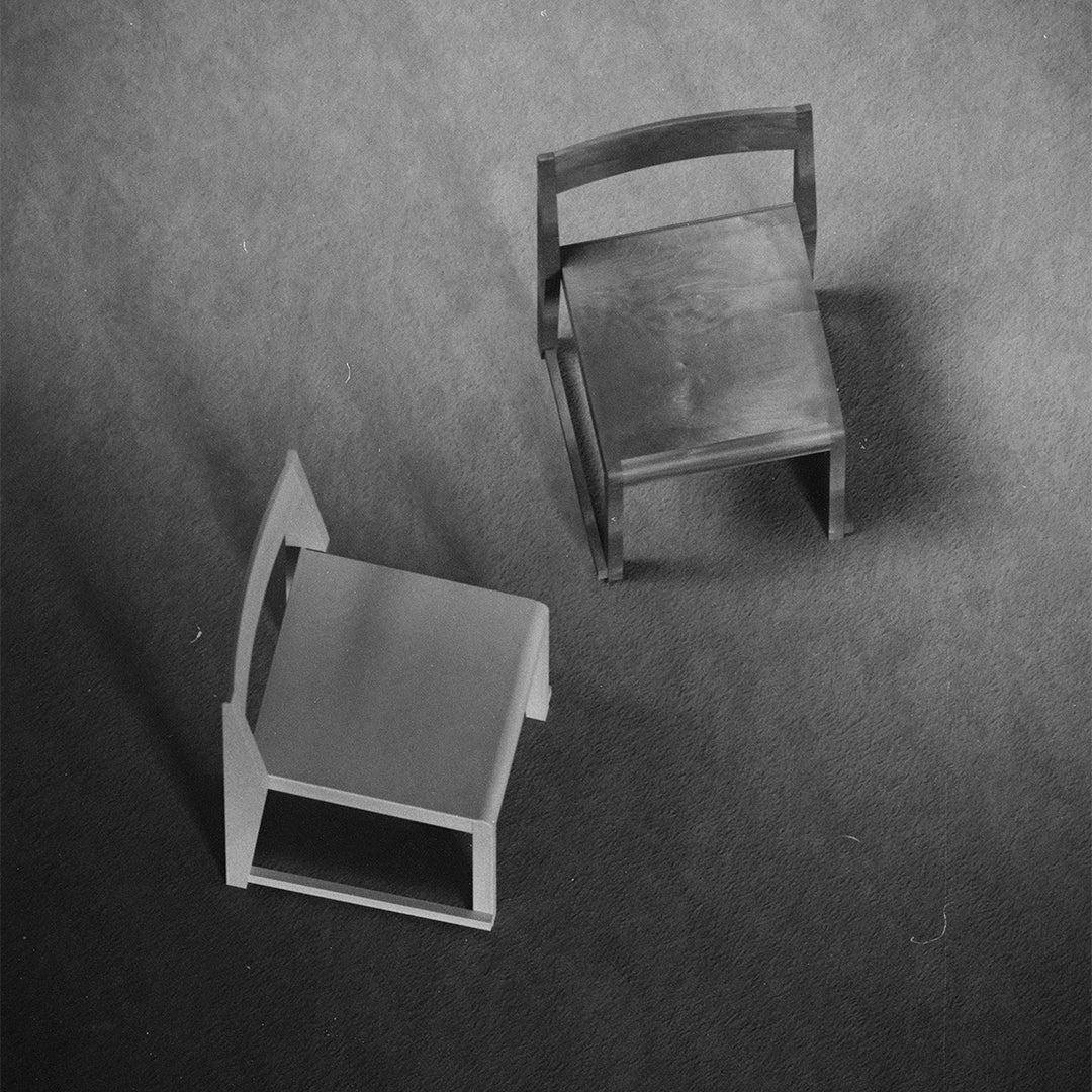 Two minimalist chairs in contrasting black and gray tones with smooth surfaces and simple geometric shapes.