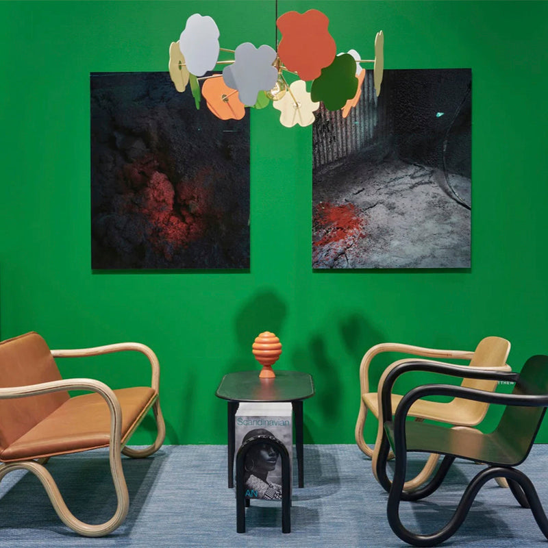 Green wall decor with dark abstract artwork, orange light fixture, and tan/black furniture set against a blue rug.