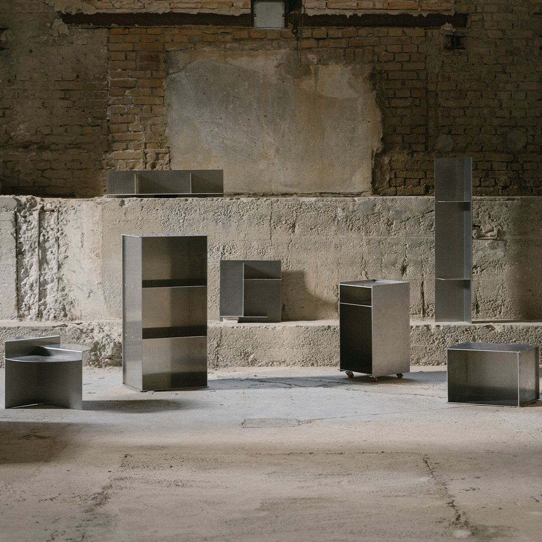 Modern minimalist furniture in brushed steel finish, featuring geometric shapes and sleek lines on a rustic backdrop.