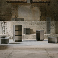 Modern minimalist furniture in brushed steel finish, featuring geometric shapes and sleek lines on a rustic backdrop.