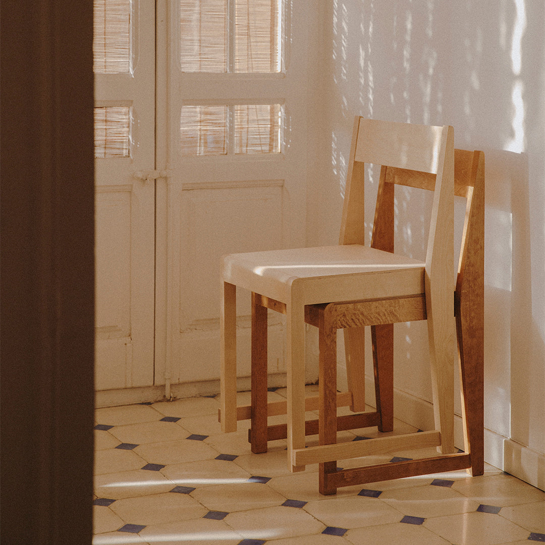 Minimalist wooden chairs in natural wood tones, set against a patterned tiled floor with blue and white accents.