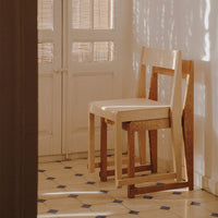 Minimalist wooden chairs in natural wood tones, set against a patterned tiled floor with blue and white accents.
