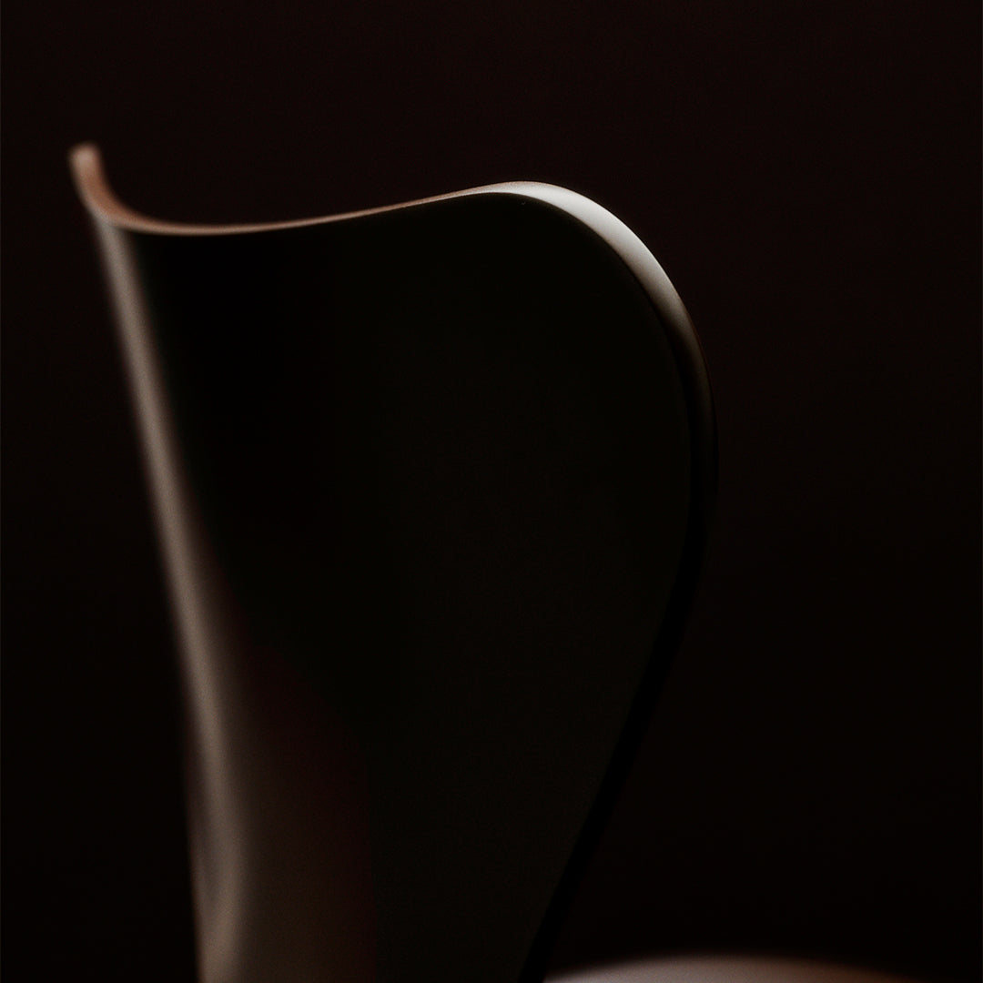 Sleek dark brown chair silhouette with smooth curves against a deep black background, emphasizing elegant design.