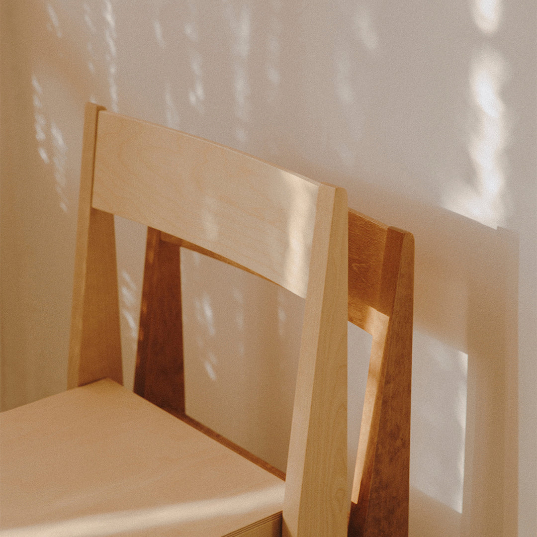 Light wood chair with a smooth finish, showcasing natural beige tones and minimalist design against a soft, shadowed backdrop.