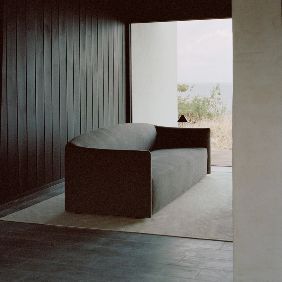 Modern black curved sofa with a smooth fabric, set against a minimalist interior featuring muted tones.